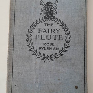 May include: A blue book cover with a black and white illustration of a fairy with wings and a wreath of leaves around the text "The Fairy Flute" by Rose Fyleman. The book is labeled "School Edition".