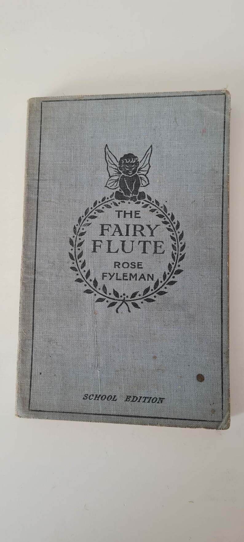 May include: A blue book cover with a black and white illustration of a fairy with wings and a wreath of leaves around the text "The Fairy Flute" by Rose Fyleman. The book is labeled "School Edition".
