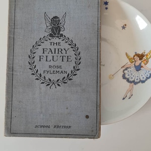 May include: A blue book with the title "The Fairy Flute" by Rose Fyleman. The book is a school edition.