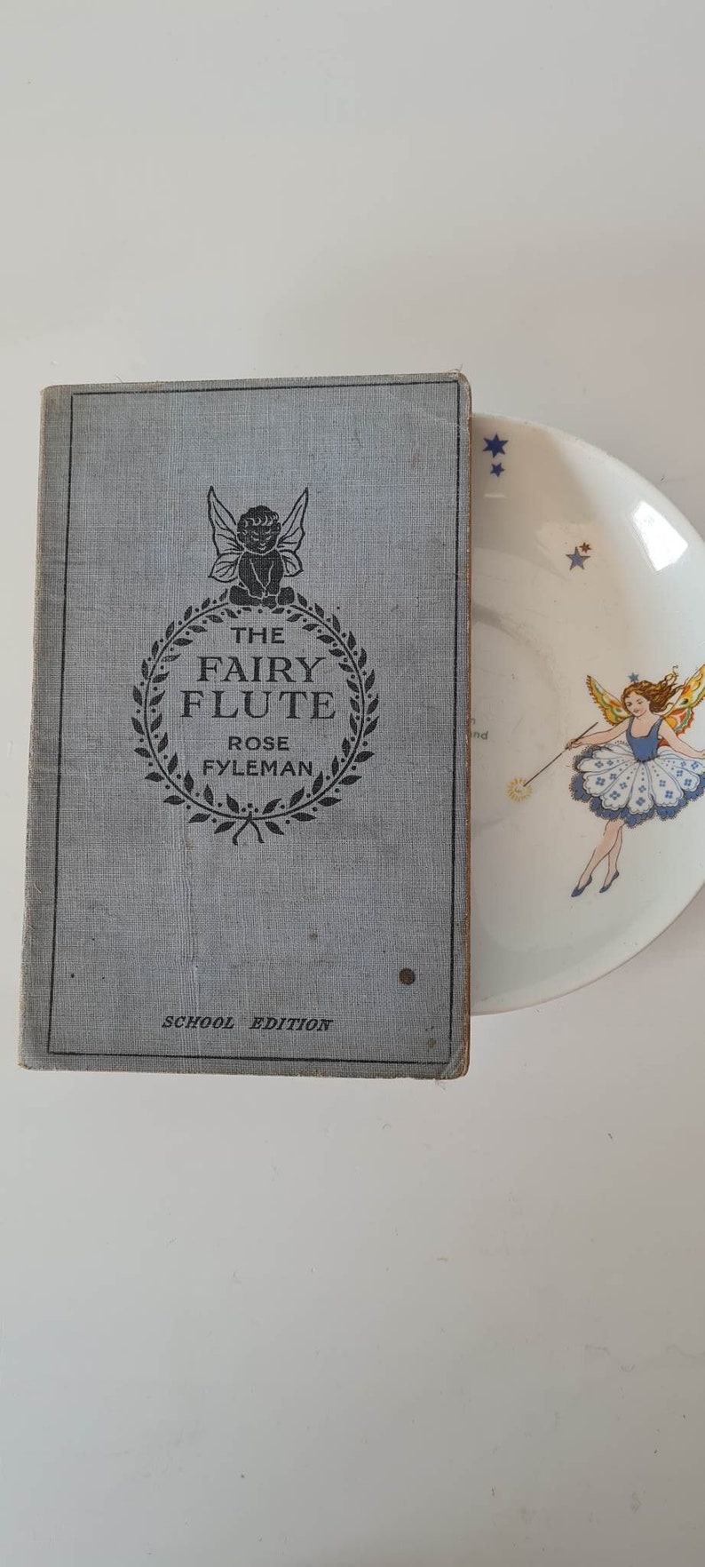 May include: A blue book with the title "The Fairy Flute" by Rose Fyleman. The book is a school edition.