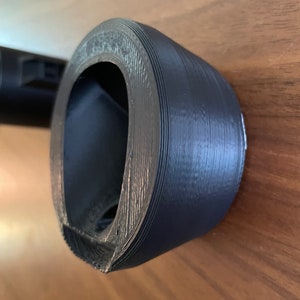 May include: A dark gray 3D printed object with a circular opening. The object is made of plastic and has a smooth, matte finish.