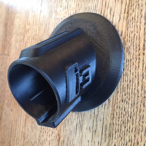 May include: A black 3D printed object with a circular base and a cylindrical tube. The tube has a slot on one side and the base has the number "13" printed on it.