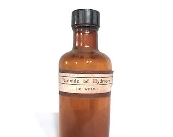 May include: A brown glass bottle with a black plastic lid. The bottle has a white label that reads "Peroxide of Hydrogen (10 VOLS.)".