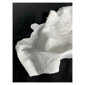 May include: White cotton handkerchief with a delicate floral embroidery design. The handkerchief features the word "ungaro" embroidered in the centre.