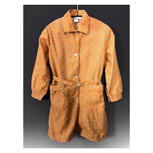 Könnte beinhalten: Ein einteiliger Overall im Vintage-Stil in einem warmen Orangeton, verziert mit einem sich wiederholenden Muster aus kleinen weißen und tealfarbenen Quadraten. Der Overall hat einen Kragen, lange Ärmel, einen Taillengürtel und Knopfverschlüsse. Er hat zwei Vordertaschen.