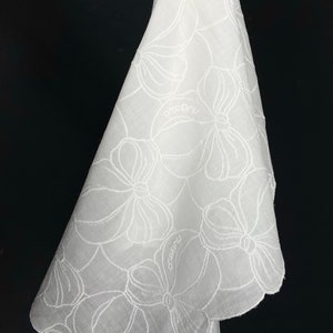 May include: White cotton handkerchief with a scalloped edge and embroidered floral design. The handkerchief has the word "ocrebru" embroidered on it.