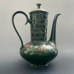 Puede incluir: Una tetera de cerámica verde oscuro con un diseño floral. La tetera tiene un patrón en relieve en el cuerpo y una tapa con un pomo.