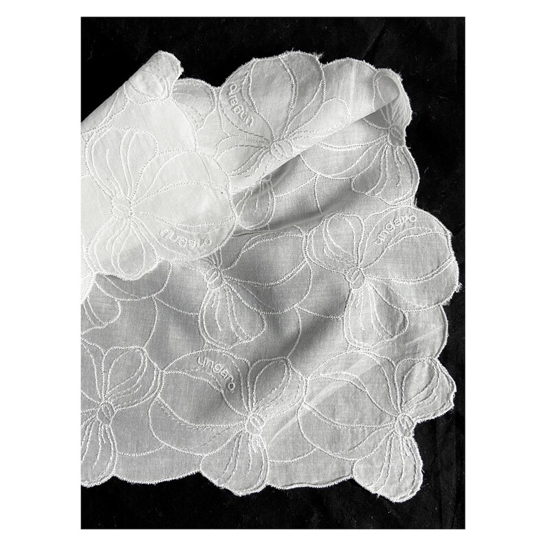May include: White cotton handkerchief with a delicate floral embroidery pattern. The handkerchief has the word "ungaro" embroidered in the corner.