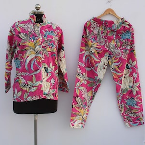 Peut inclure: Un ensemble de pyjama rose vif, orn&eacute; d'un imprim&eacute; color&eacute; de motifs botaniques et d'oiseaux. L'ensemble comprend une chemise boutonn&eacute;e &agrave; manches longues et un pantalon assorti. La chemise est pr&eacute;sent&eacute;e sur un mannequin, le pantalon sur un cintre en bois.