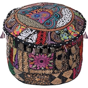Puede incluir: Puf redondo de patchwork con base negra y parte superior bordada colorida. La parte superior presenta un medallón central con diseños florales y paisley en tonos rosa, azul y dorado. Los lados están adornados con borlas.