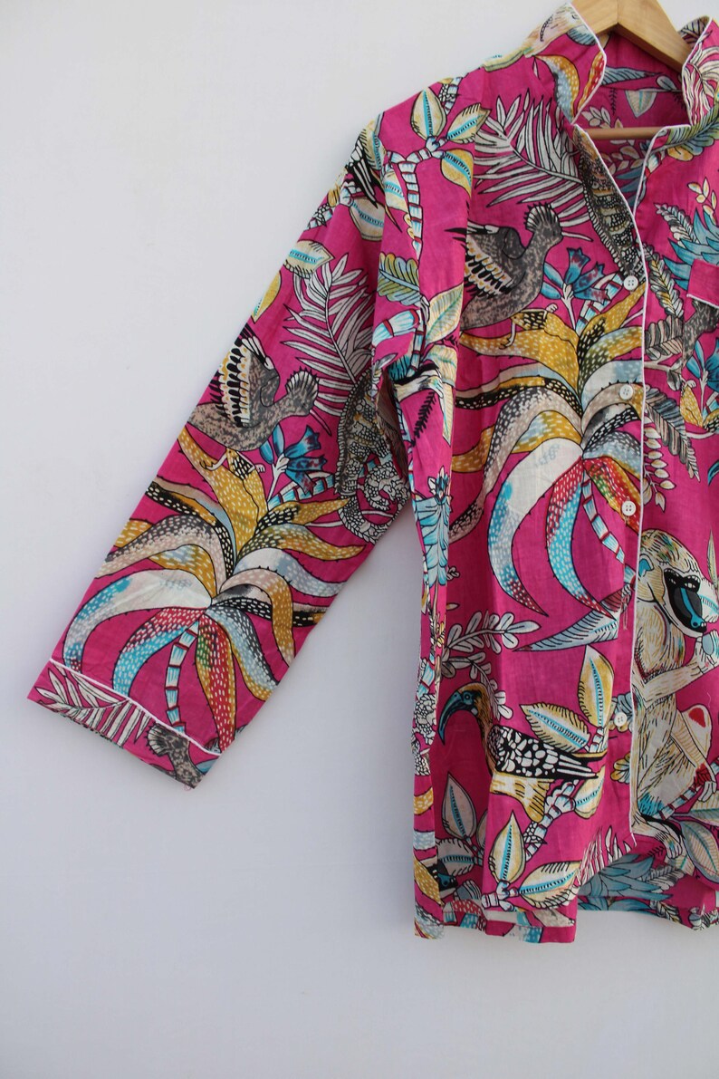 Peut inclure: Un ensemble de pyjama rose vif avec un imprim&eacute; botanique et animalier. Le haut &agrave; manches longues et le pantalon pr&eacute;sentent un motif color&eacute; d'oiseaux, de feuilles et d'autres &eacute;l&eacute;ments de la flore et de la faune. Une bordure blanche souligne les bords du v&ecirc;tement.