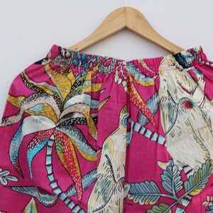 Peut inclure: Tissu rose vif avec un imprim&eacute; tropical vibrant de palmiers, d'oiseaux et de feuillage dans des tons de jaune, bleu et blanc. Le tissu est fronc&eacute; en haut, sugg&eacute;rant un v&ecirc;tement.