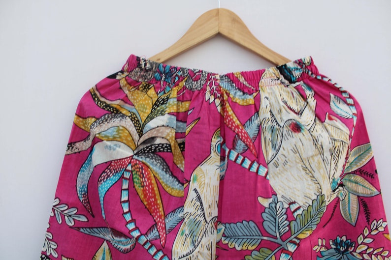 Peut inclure: Tissu rose vif avec un imprim&eacute; tropical vibrant de palmiers, d'oiseaux et de feuillage dans des tons de jaune, bleu et blanc. Le tissu est fronc&eacute; en haut, sugg&eacute;rant un v&ecirc;tement.