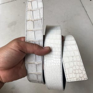 Puede incluir: Tira de cinturón de piel de cocodrilo blanca. La tira está hecha de piel de cocodrilo genuina y tiene un color blanco. La tira está cosida con hilo blanco.