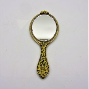 May include: A gold-toned hand mirror with an oval-shaped mirror and a handle decorated with yellow flowers.