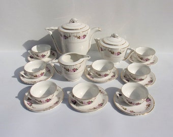 May include: A vintage porcelain tea set with a floral design. The set includes a teapot, sugar bowl, creamer, and several teacups with saucers. The set is white with gold trim and pink and purple floral accents.