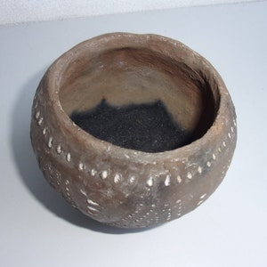 Op de afbeelding: Een kleine, ronde, bruine kleipot met een wit gevlekt ontwerp. De pot is leeg en heeft een donkerbruine binnenkant.