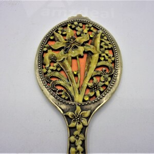 May include: A vintage hand mirror with a floral design. The mirror is made of metal and has a gold finish. The floral design is in shades of yellow and orange and features a large flower in the center.