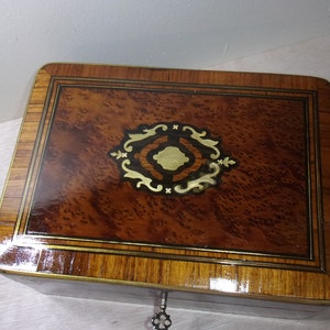 May include: A wooden box with a decorative inlay of gold and black. The box has a brass lock and keyhole.