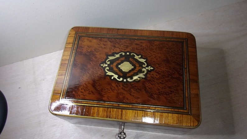 May include: A wooden box with a decorative inlay of gold and black. The box has a brass lock and keyhole.