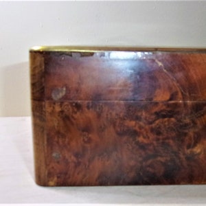 May include: A wooden box with a brass trim. The box has a dark brown wood grain pattern.