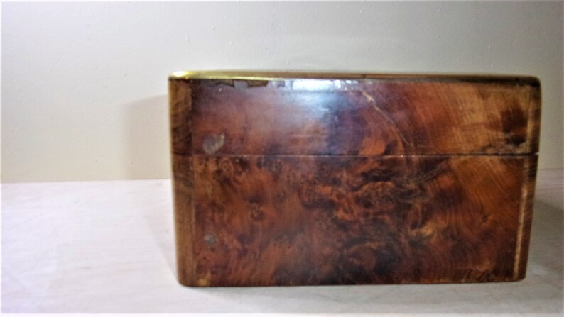 May include: A wooden box with a brass trim. The box has a dark brown wood grain pattern.