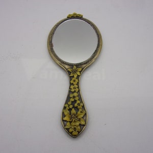 May include: A vintage hand mirror with a gold-tone frame and a floral design. The mirror has a round shape and a handle with a floral design.