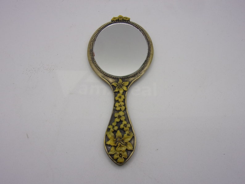 May include: A vintage hand mirror with a gold-tone frame and a floral design. The mirror has a round shape and a handle with a floral design.