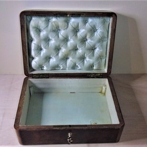 May include: An open wooden box with a light blue satin lining. The lining has a tufted design. The box has a brass lock and keyhole.