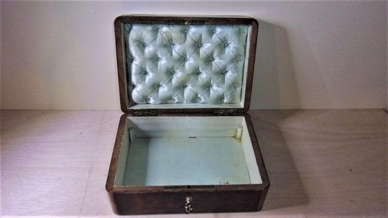 May include: An open wooden box with a light blue satin lining. The lining has a tufted design. The box has a brass lock and keyhole.