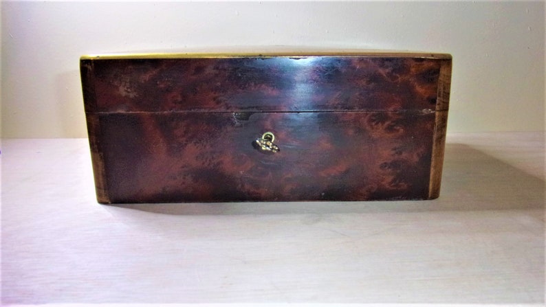 May include: A dark brown wooden box with a brass trim and a brass latch. The box has a wood grain pattern.