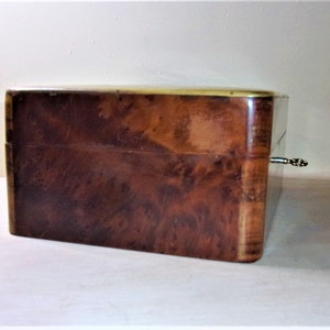 May include: A wooden box with a brass trim and a keyhole. The box has a dark brown wood grain pattern.