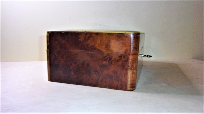 May include: A wooden box with a brass trim and a keyhole. The box has a dark brown wood grain pattern.