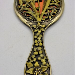 May include: A vintage hand mirror with a floral design. The mirror is round and has a metal frame with a floral pattern. The handle is also decorated with flowers.