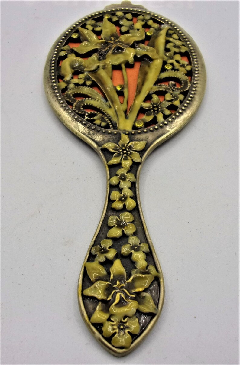 May include: A vintage hand mirror with a floral design. The mirror is round and has a metal frame with a floral pattern. The handle is also decorated with flowers.