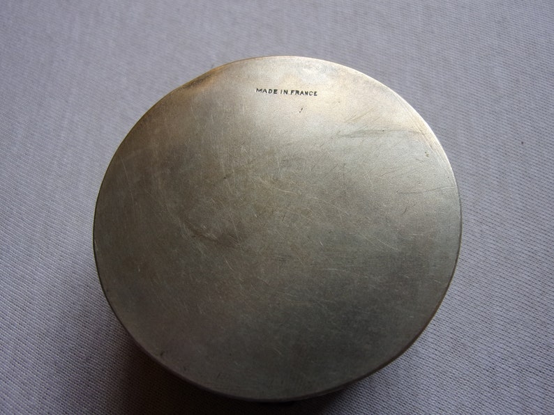 May include: A silver round metal box with the words "Made in France" engraved on the bottom.