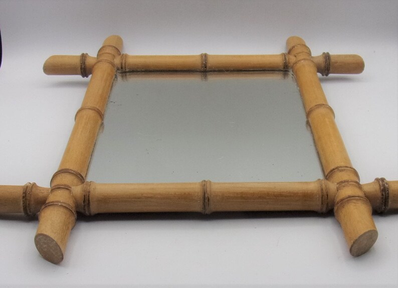 Puede incluir: Un espejo rectangular con un marco de bamb&uacute; natural. El marco est&aacute; hecho de piezas de bamb&uacute; redondas y gruesas que se unen en las esquinas. El espejo es transparente y refleja el entorno circundante.