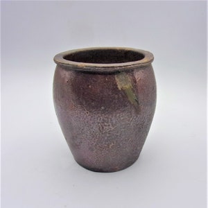 May include: A small, brown, glazed ceramic pot with a rounded body and a slightly flared rim.