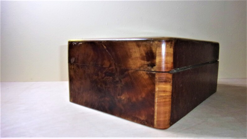 May include: A wooden box with a dark brown finish and a light brown wood trim. The box has a hinged lid and a smooth surface.