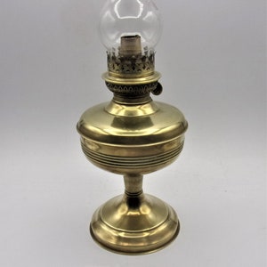 Puede incluir: Una l&aacute;mpara de aceite de lat&oacute;n con una chimenea de vidrio transparente y una base decorativa. La l&aacute;mpara tiene un dise&ntilde;o sencillo y est&aacute; en buen estado.