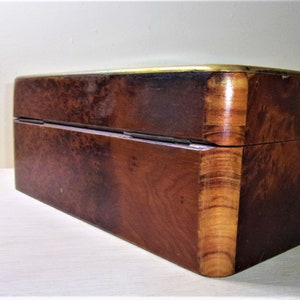 May include: A wooden box with a brass trim. The box has a dark brown finish and a wood grain pattern. The box is closed and has a hinged lid.