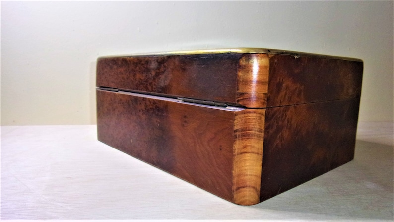 May include: A wooden box with a brass trim. The box has a dark brown finish and a wood grain pattern. The box is closed and has a hinged lid.