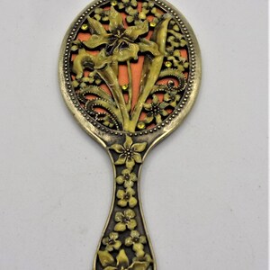 May include: A vintage hand mirror with a floral design. The mirror is made of metal and has a gold finish. The handle is decorated with flowers and leaves. The mirror is oval shaped and has a small, round mirror in the center.