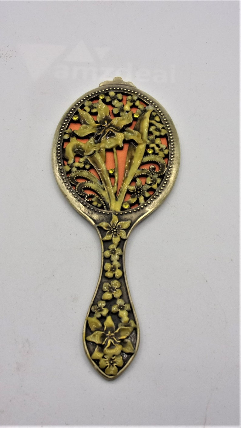 May include: A vintage hand mirror with a floral design. The mirror is made of metal and has a gold finish. The handle is decorated with flowers and leaves. The mirror is oval shaped and has a small, round mirror in the center.