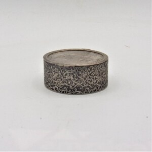 May include: A silver round trinket box with an intricate floral design.