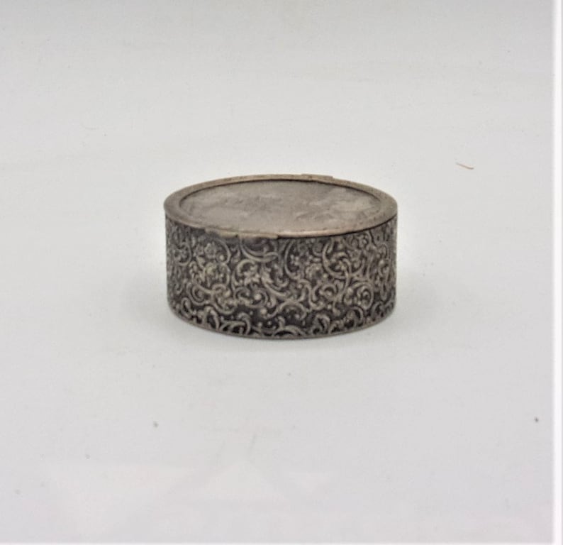 May include: A silver round trinket box with an intricate floral design.