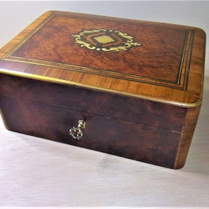 May include: A wooden box with a brass lock and keyhole. The top of the box is made of wood with a marquetry design. The box is closed.