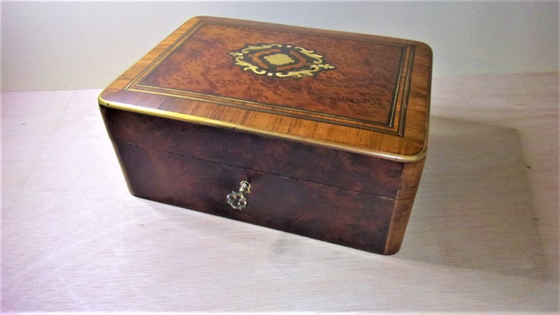 May include: A wooden box with a brass lock and keyhole. The top of the box is made of wood with a marquetry design. The box is closed.