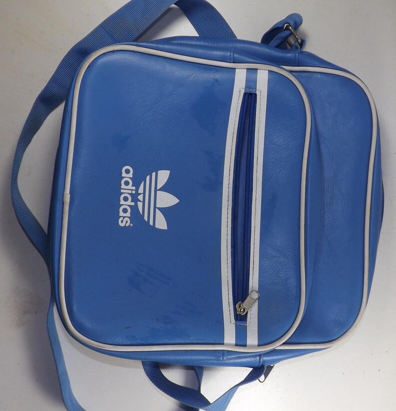 May include: A blue Adidas shoulder bag with a white zipper and white Adidas logo. The bag has a white stripe down the side.