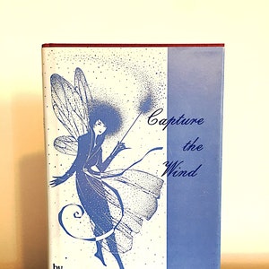 May include: A book cover with a blue and white illustration of a fairy with wings. The text on the cover reads "Capture the Wind" by Joy Bischof. The book is described as "A book for the young of all ages."